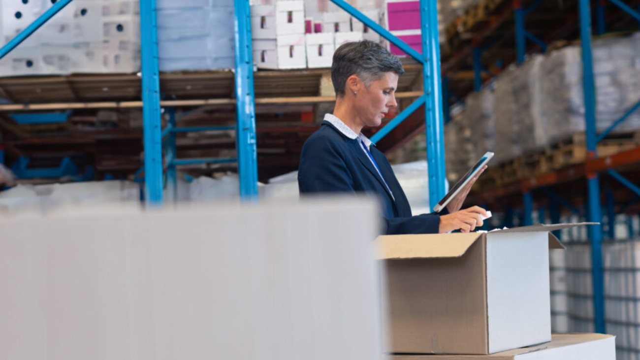 Warehouse manager using a tablet to inspect inventory, representing the use of warehouse management system software in a modern distribution facility.