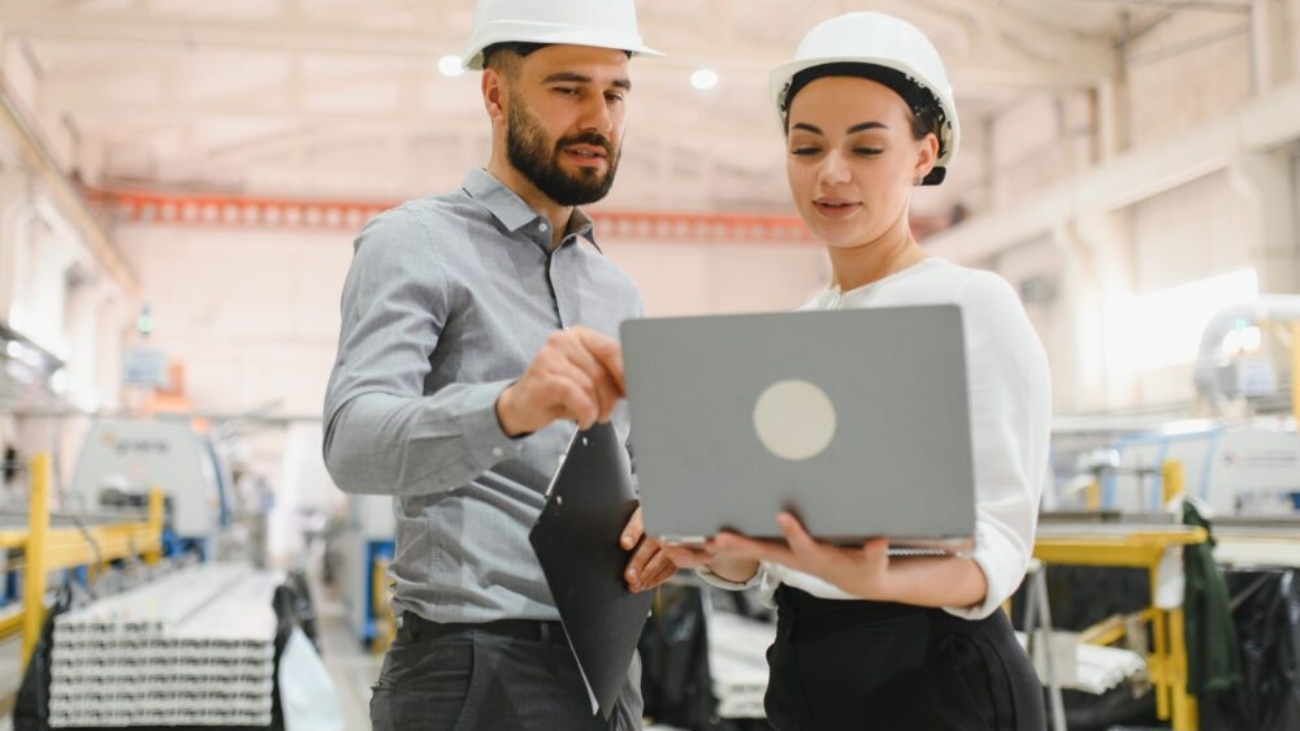 Manufacturing professionals reviewing production data on a laptop in a factory, illustrating the benefits of the Best ERP for Manufacturing with real-time visibility and operational control.