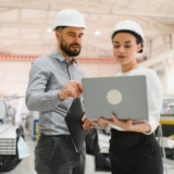 Manufacturing professionals reviewing production data on a laptop in a factory, illustrating the benefits of the Best ERP for Manufacturing with real-time visibility and operational control.
