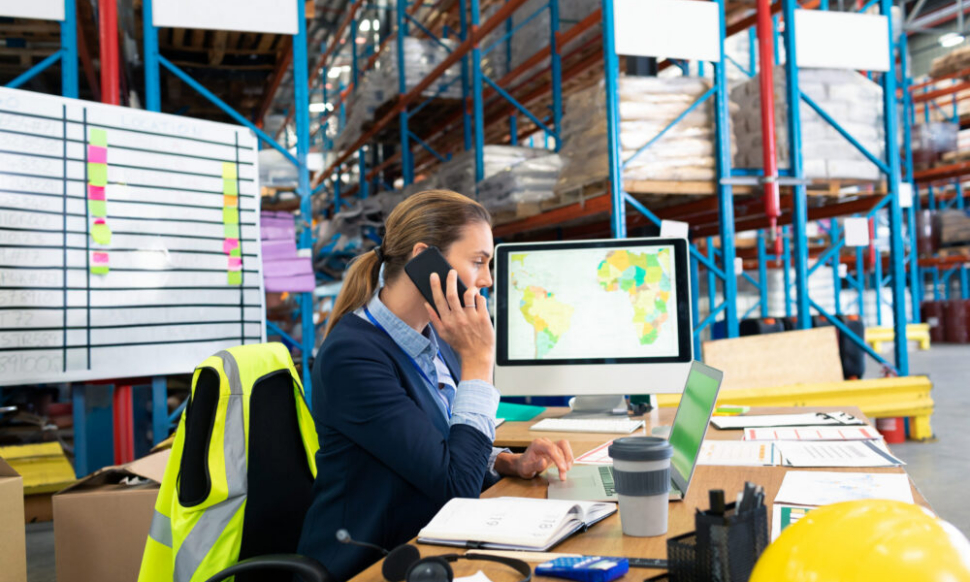 Businesswoman in warehouse on phone using NetSuite warehouse management system software for real-time stock and order management