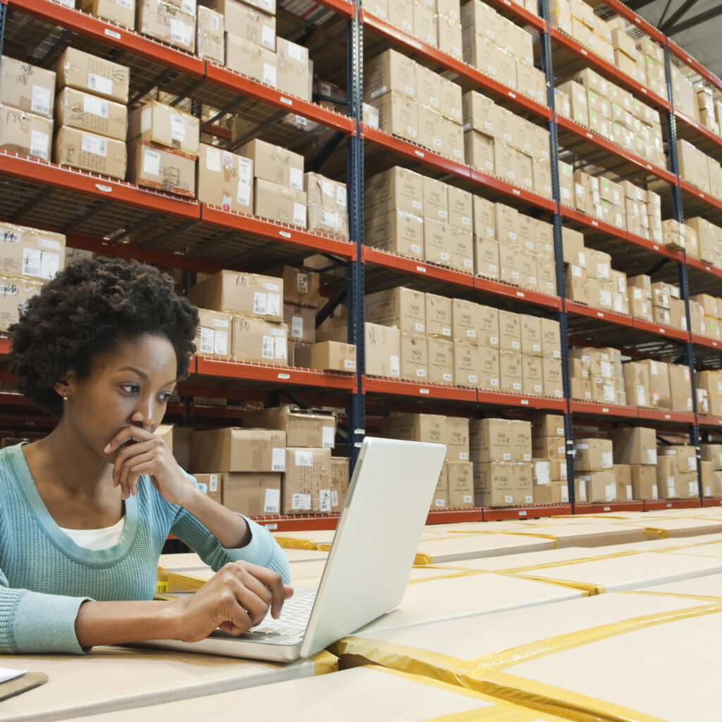 Female warehouse worker working on a laptop in a warehouse office