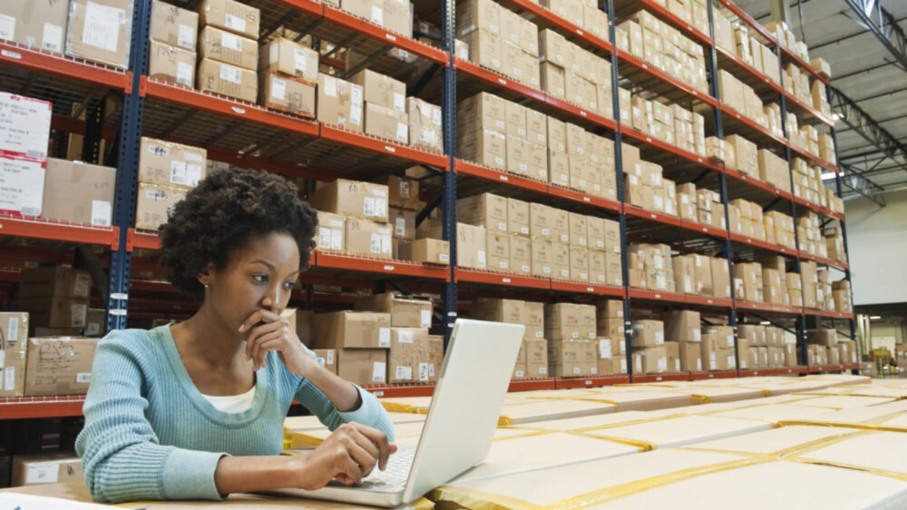 Female warehouse worker working on a laptop in a warehouse office