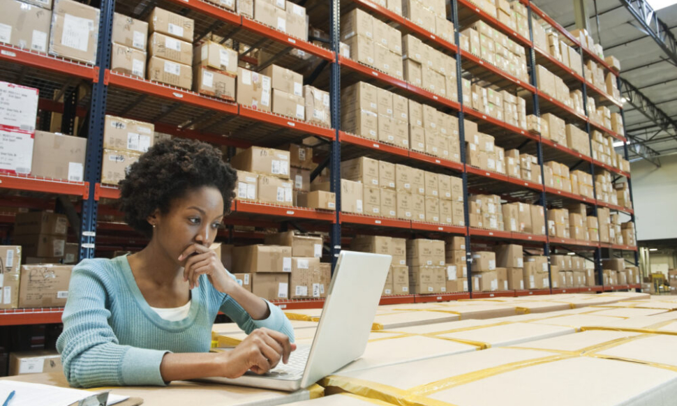 Female warehouse worker working on a laptop in a warehouse office